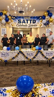 The SATTD team behind a table decorated in blue and gold balloons and stars at their 2026 Celebrate Service event